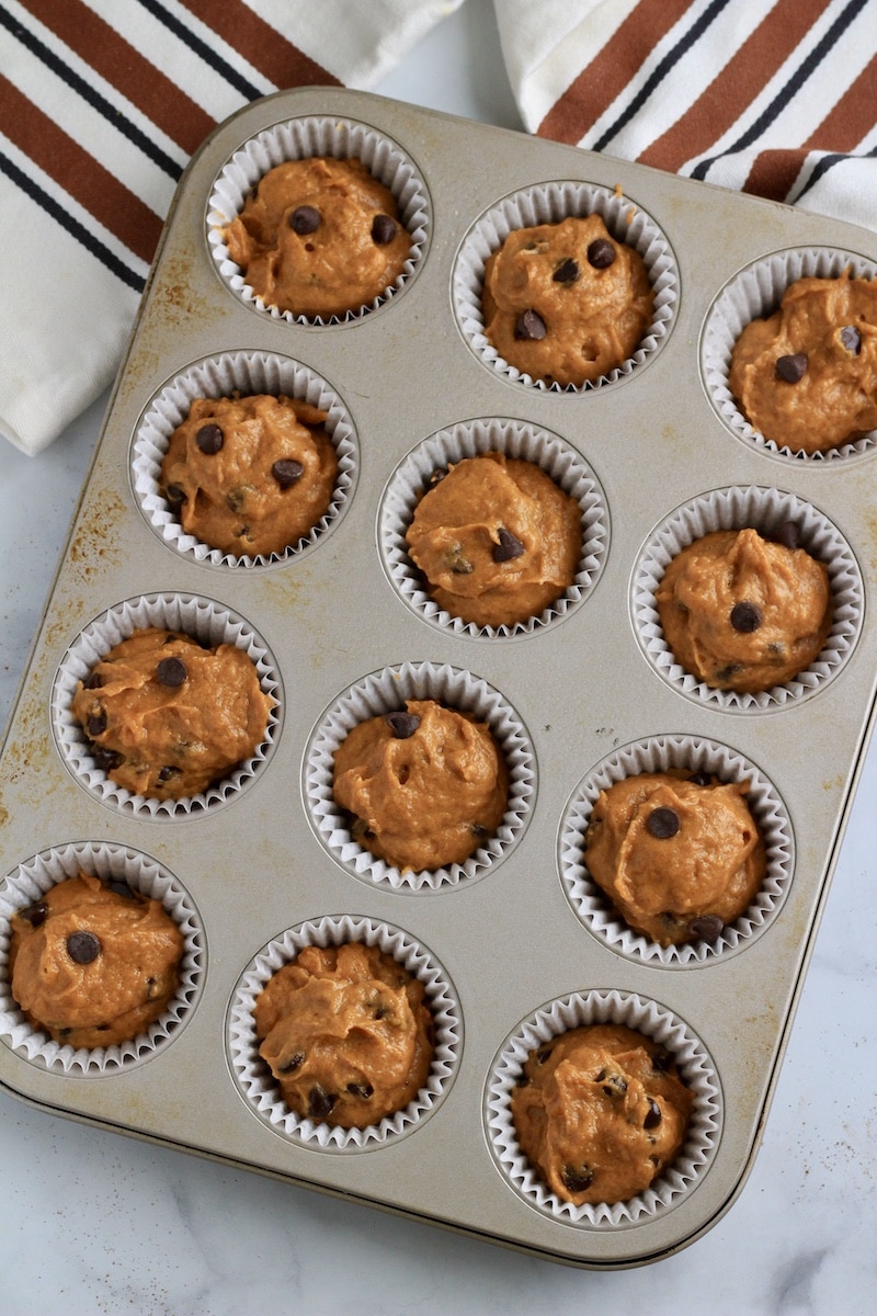 A top down photo of a standard muffin tin with unbaked chocolate chip pumpkin muffin batter.