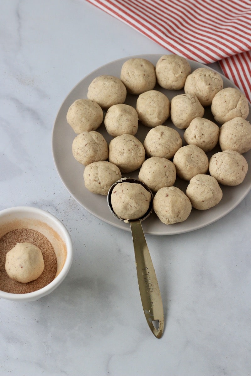 A white plate with vegan snickerdoodle cookie dough before baking and a small bowl to the left with cinnamon sugar.