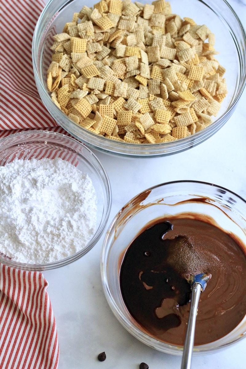 Three glass bowls one with Chex, one with powdered sugar, and one with the cookie butter chocolate mixture with vanilla and salt added.