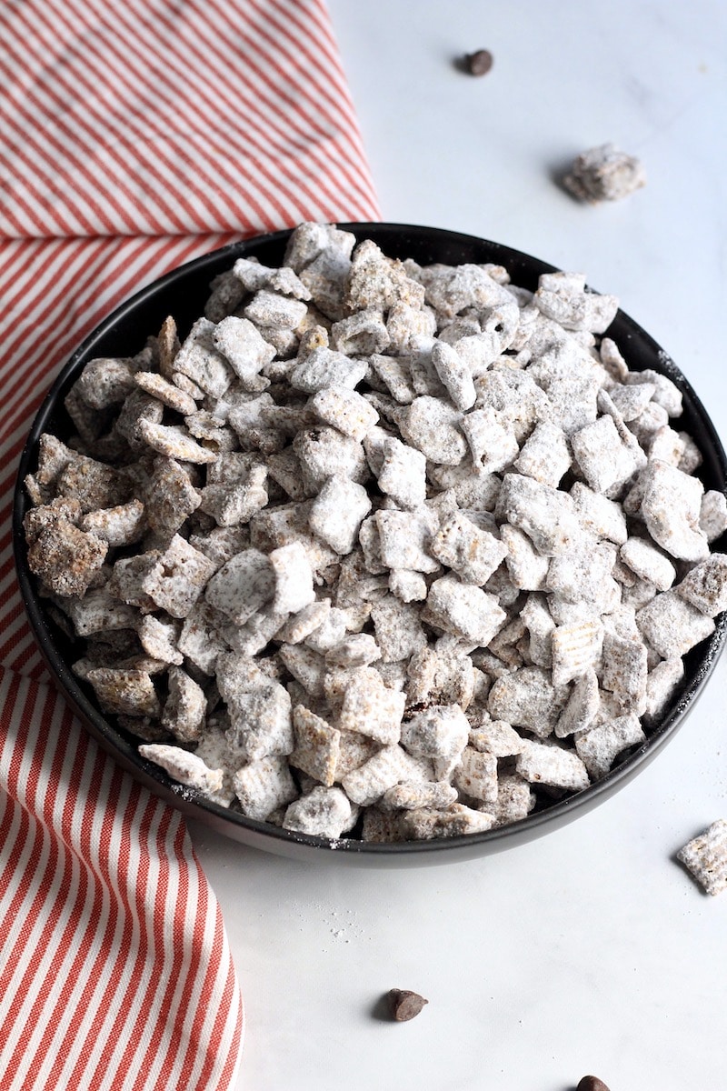 A black bowl with cookie butter muddy buddies next to a red and white striped towel.