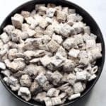 A square photo of a black bowl filled with cookie butter muddy buddies.