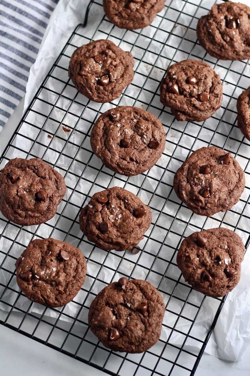 A black cooling rack with double chocolate chip cookies cooling over a white counter.