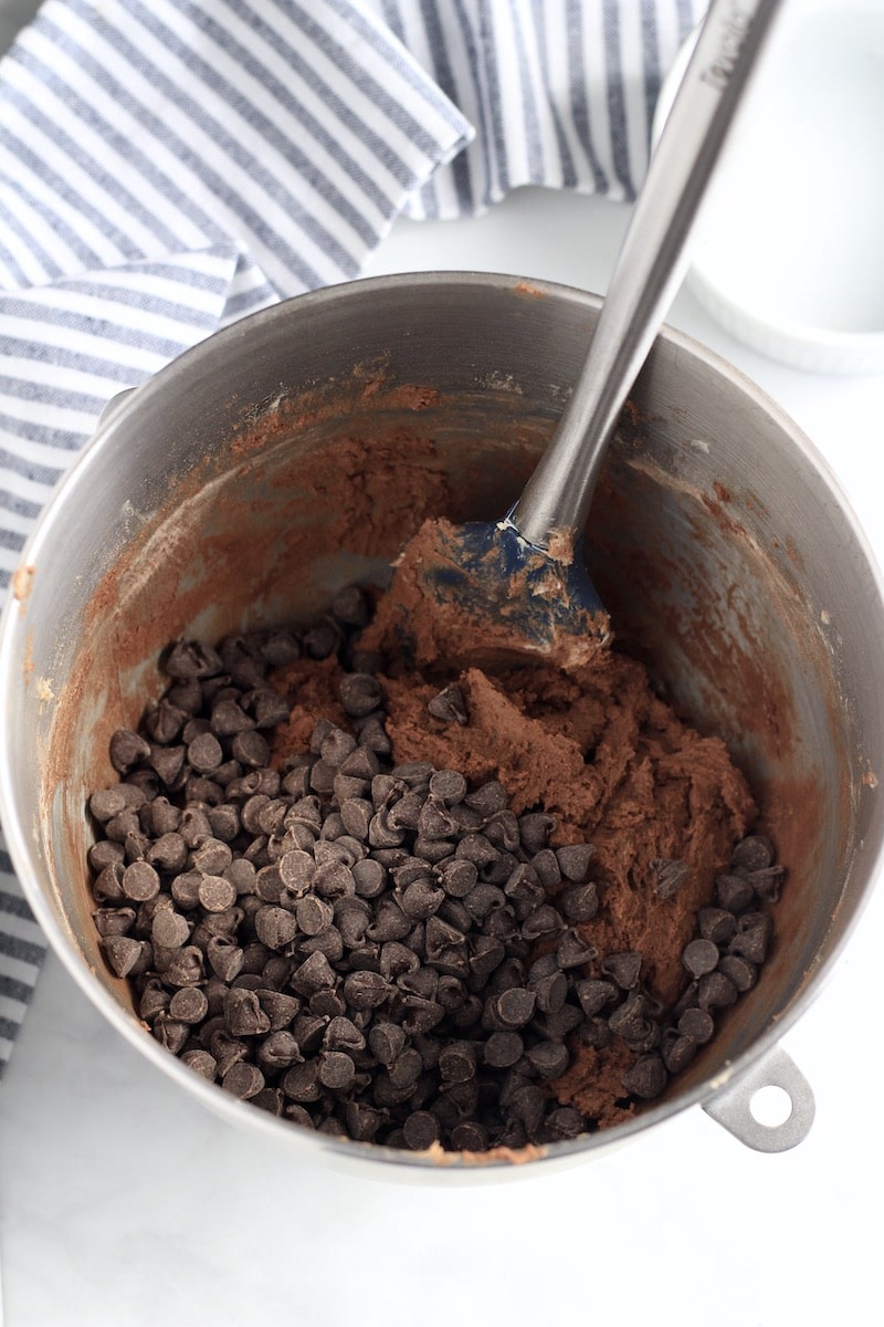 A mixing bowl with double chocolate cookie dough with a spatula before the chocolate chips are mixed in.