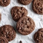 Two chocolate chocolate chip cookies on parchment paper.