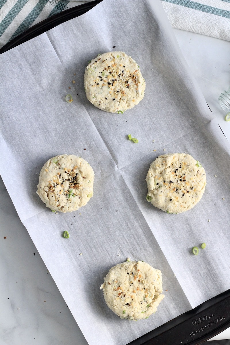 Four everything bagel scallion biscuits on a baking sheet topped with extra everything bagel seasoning.
