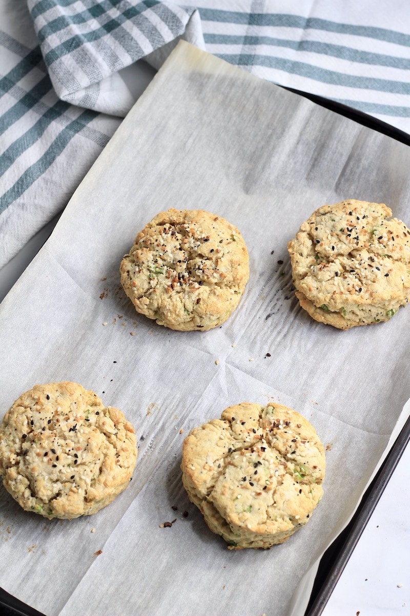 Four everything bagel scallion biscuits after baking on a piece of parchment paper.