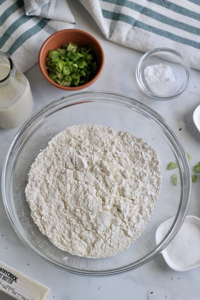 A glass bowl with the flour mixture in the middle and additional ingredients around the outside.