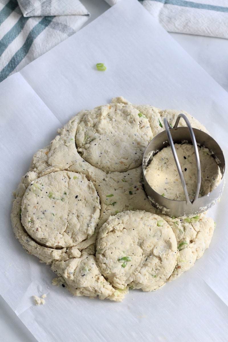 Biscuit dough on a piece of parchment paper being cut with a biscuit cutter.