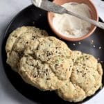 A square photo of everything bagel scallion biscuits on a black plate with cream cheese in a small bowl in the back.