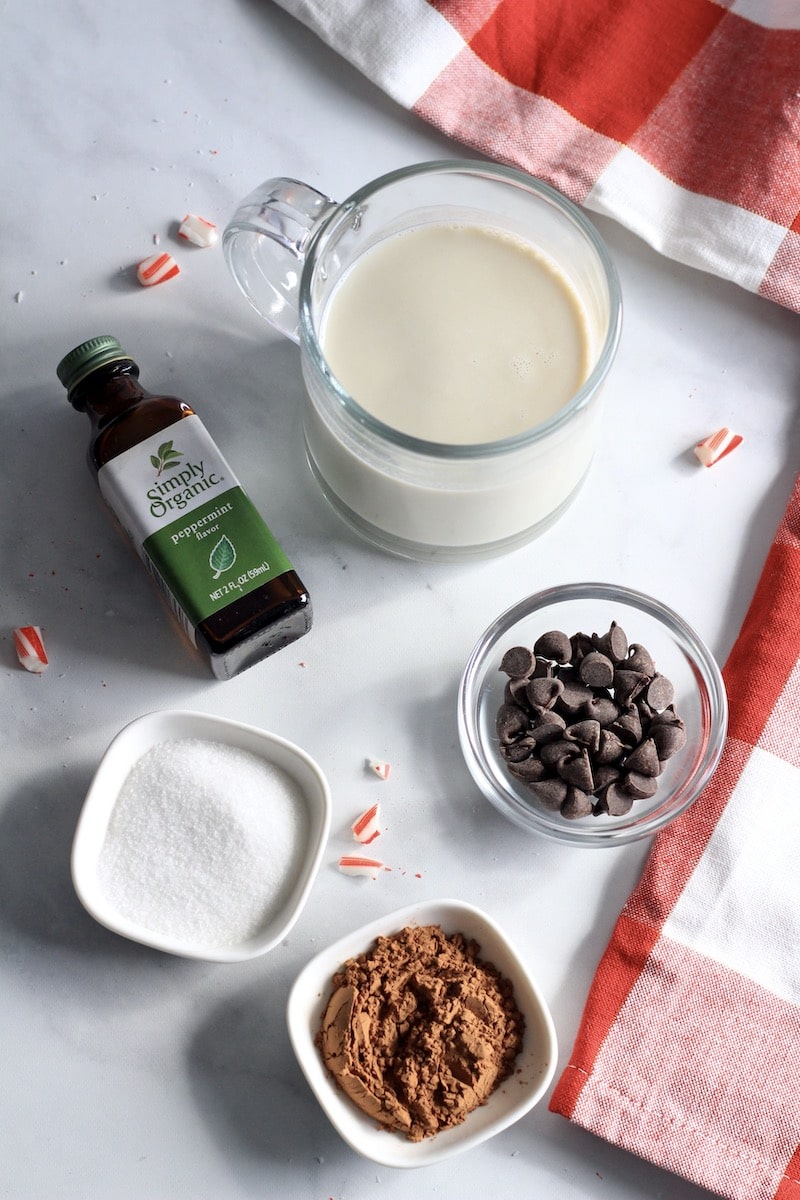 Ingredients for peppermint hot chocolate on a white counter with a red and white towel to the right.