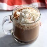 A clear glass mug of peppermint hot cocoa on a white counter.