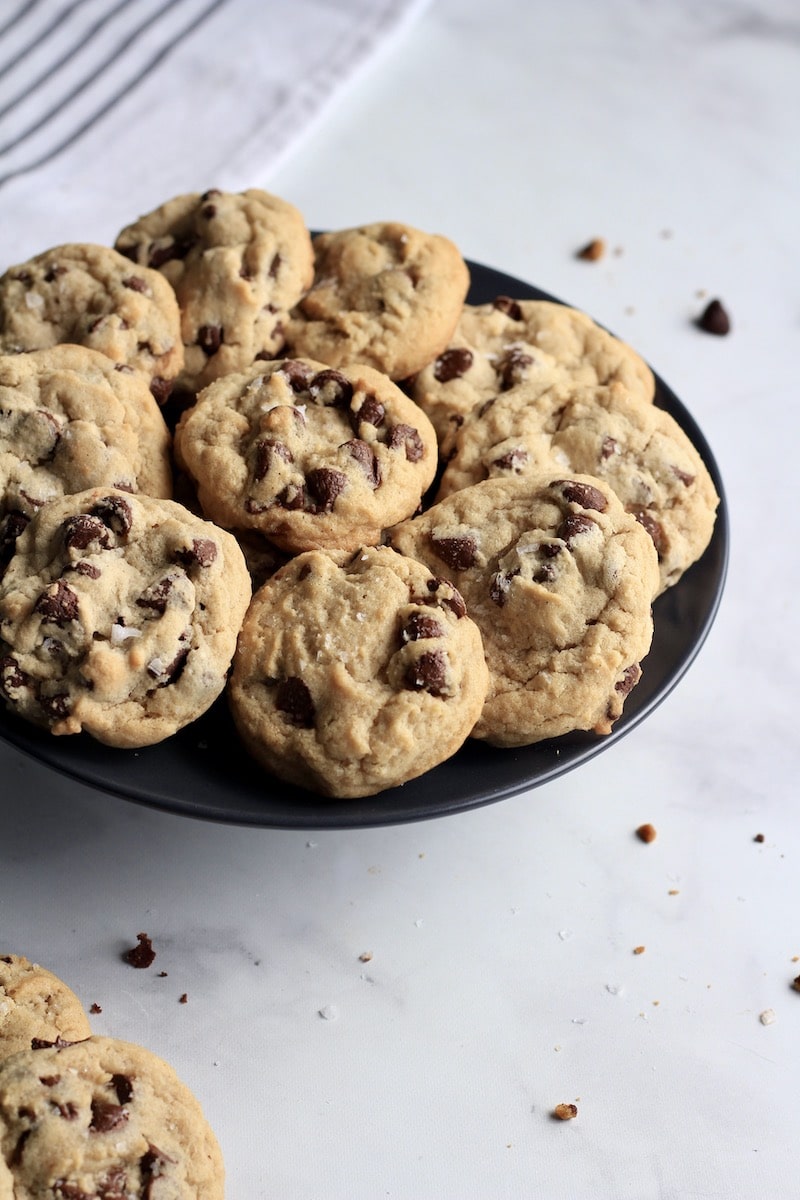 A blue plate in the middle with chocolate chip cookies and some crumbs on the counter.
