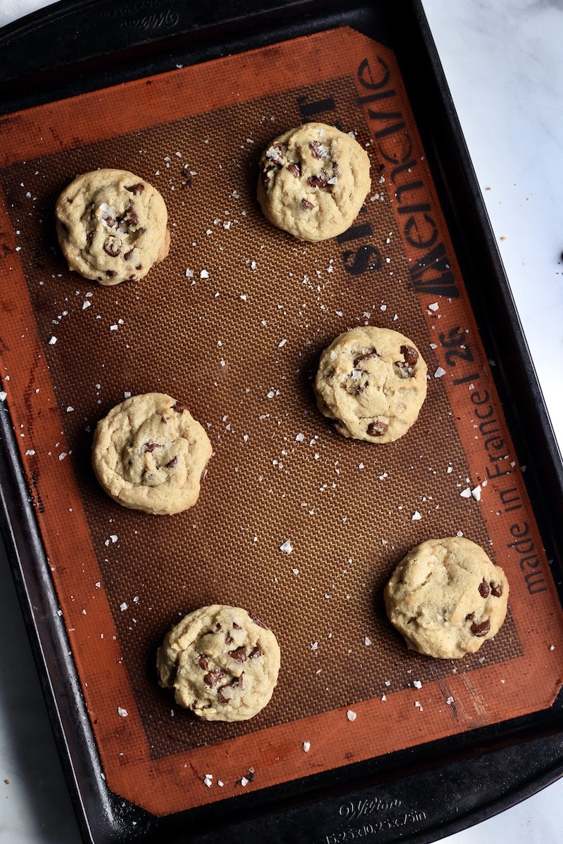 A rimmed baking sheet with a silicone baking mat and chocolate chip cookies after baking.