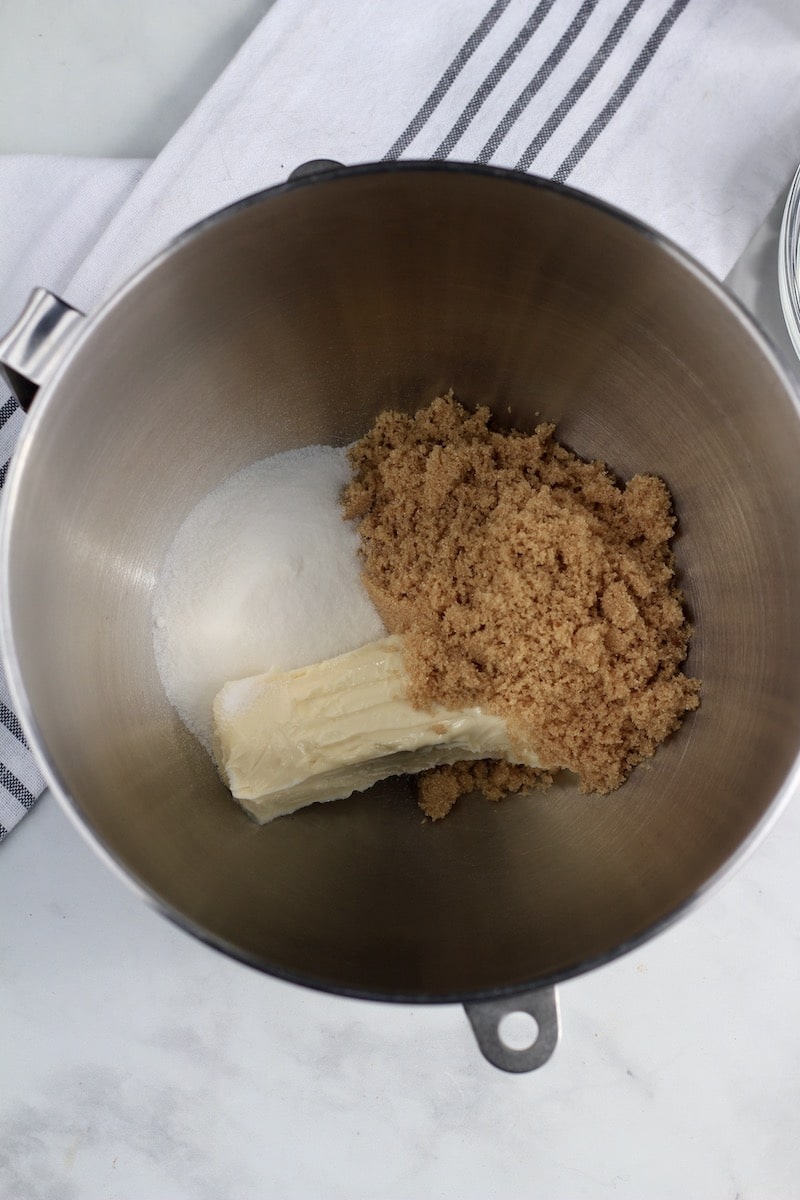 A silver mixing bowl with granulated sugar, brown sugar, and plant-based butter before mixing.