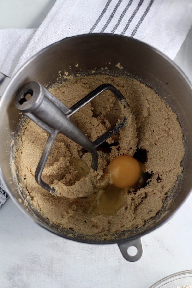 A silver mixing bowl with butter and sugar creamed and an egg and vanilla added in.