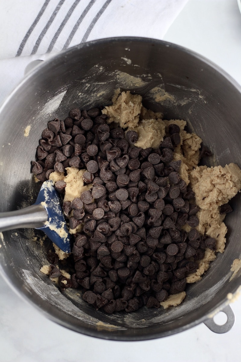 A silver mixing bowl with cookie dough topped with chocolate chips before mixing.