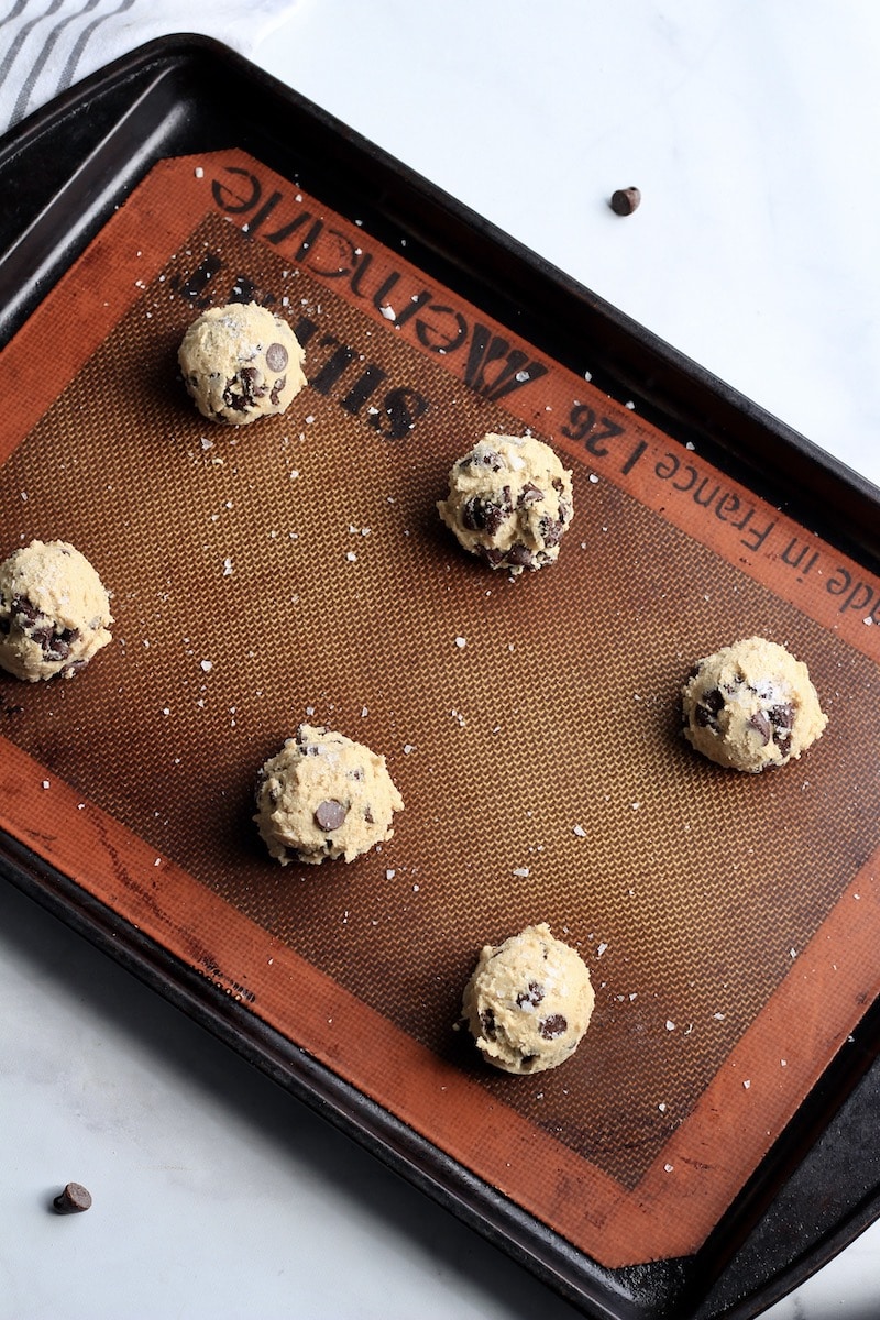 A rimmed baking sheet with balls of chocolate chip cookie dough.