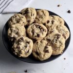 A plate of chocolate chip cookies with some crumbs on the counter.