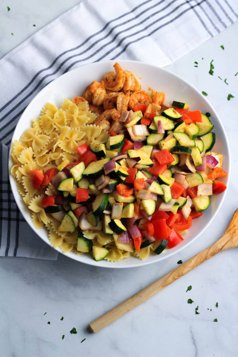 A white bowl with shrimp and vegetable pasta before being stirred.