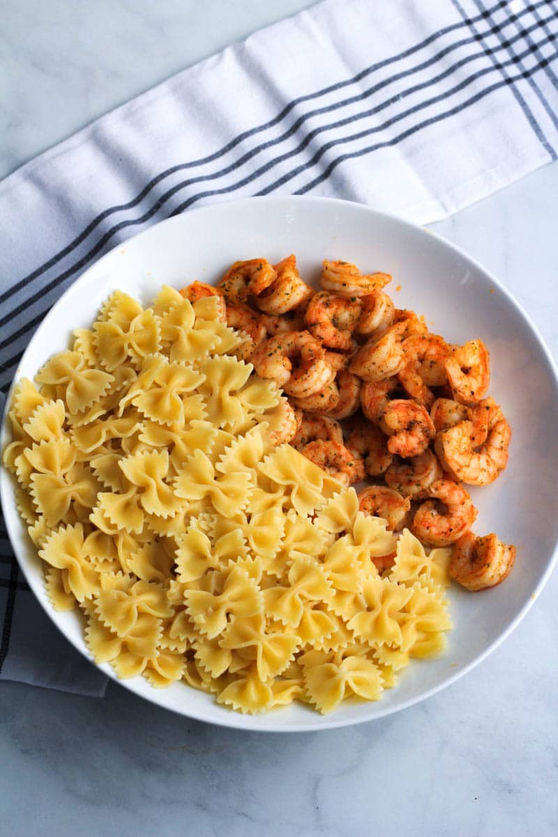A white bowl with bow tie pasta on the left and cooked shrimp on the right.