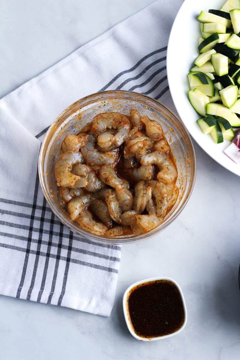 A glass bowl with the shrimp marinading and an extra bowl with left over dressing.