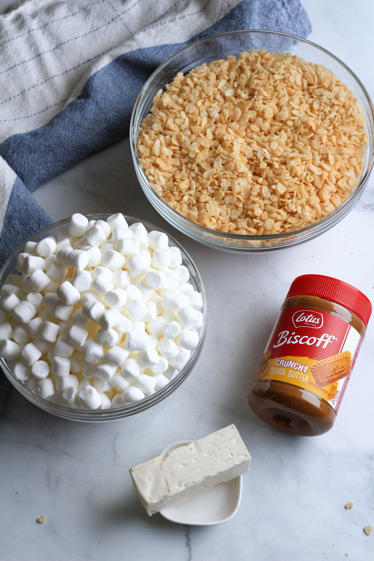 The ingredients for cookie butter rice krispie treats on a white counter with a blue and white dish towel in the back.