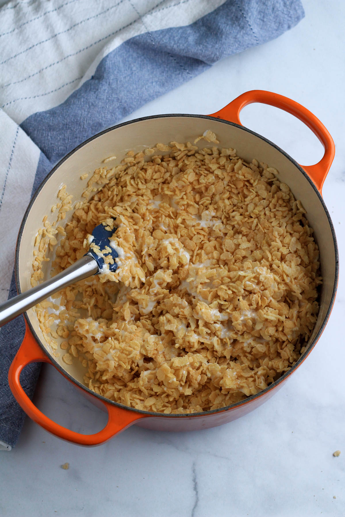 A large orange pot with rice krispie cereal mixed with melted marshmallows.