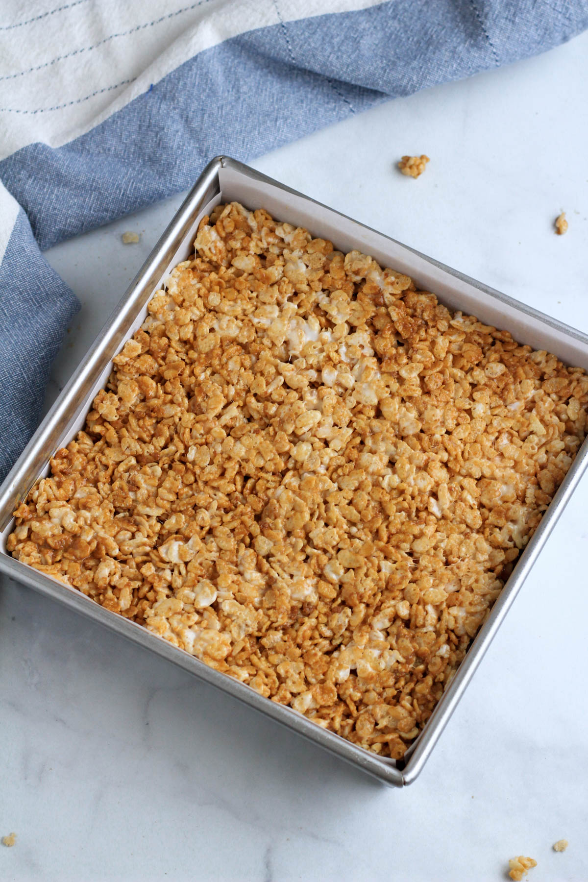 Cookie butter rice krispie treats pressed into an 8x8 pan with parchment paper.