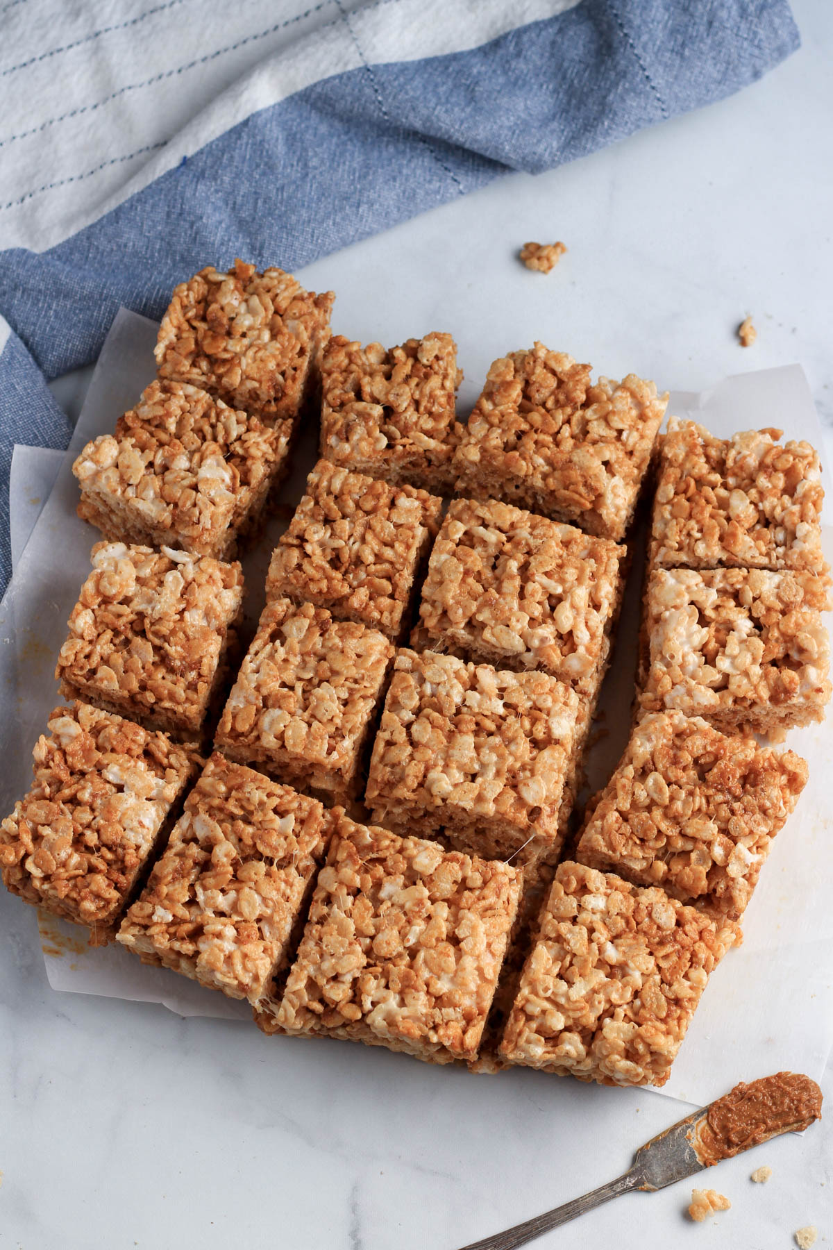 A four by four grid of cookie butter rice krispie treats on parchment paper with a small knife with cookie butter in the front.