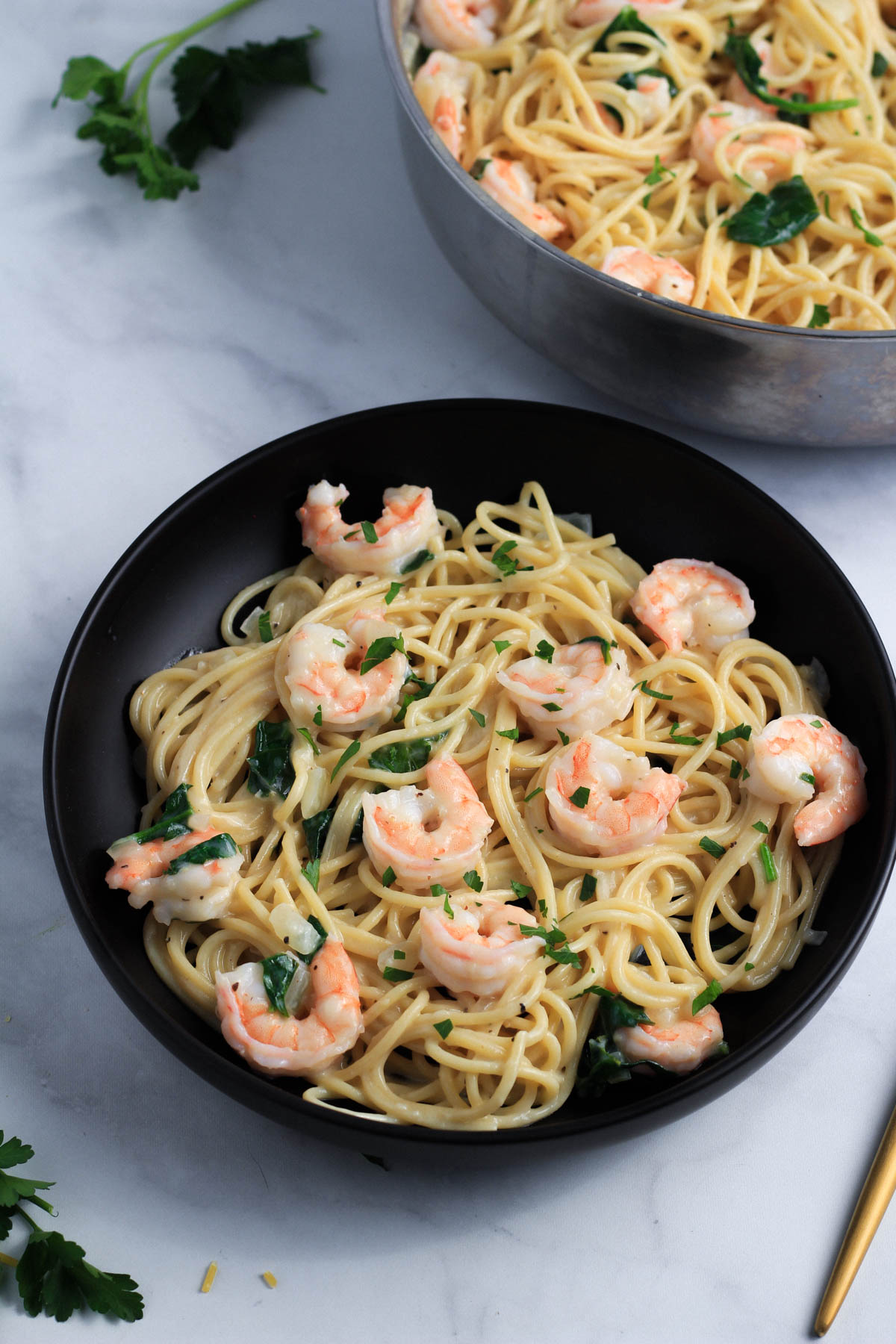 A black bowl with creamy garlic shrimp pasta and a skillet in the back.