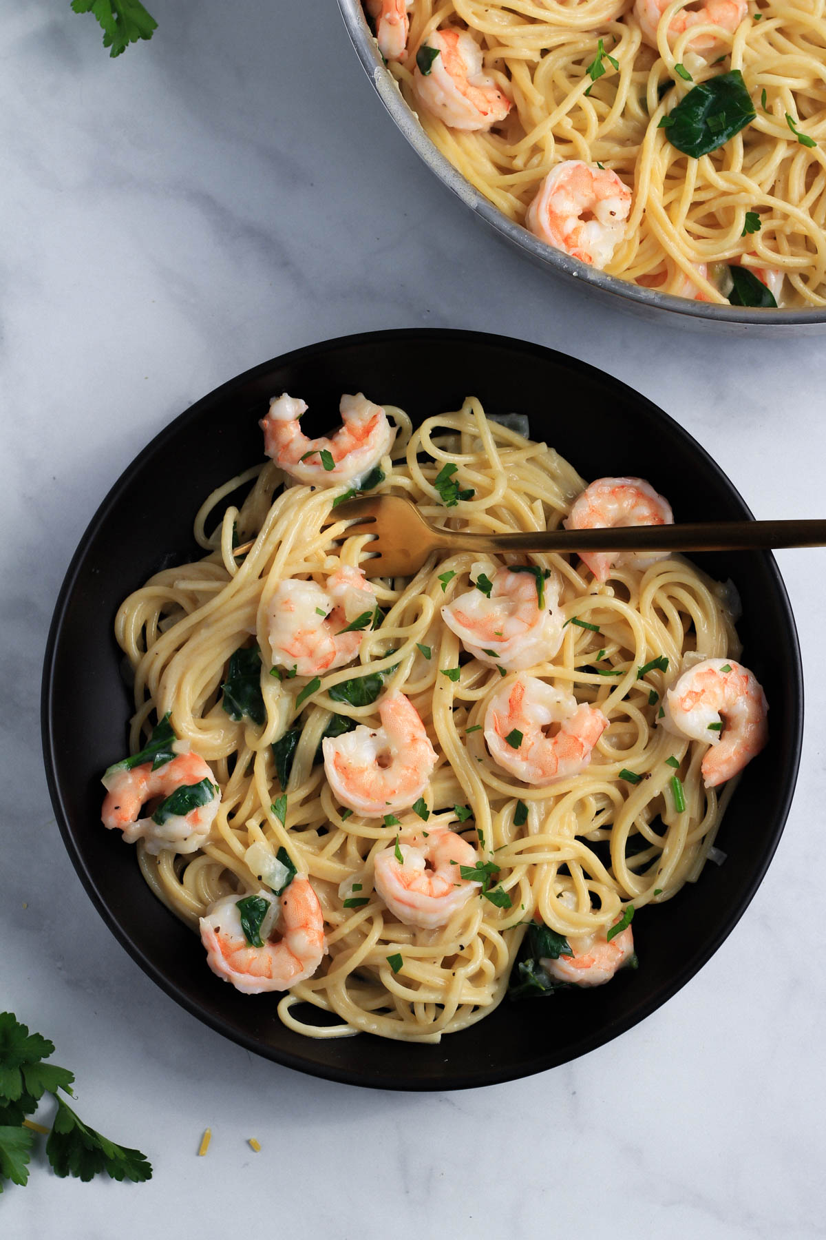 A black bowl with a gold fork in the creamy garlic pasta with shrimp.