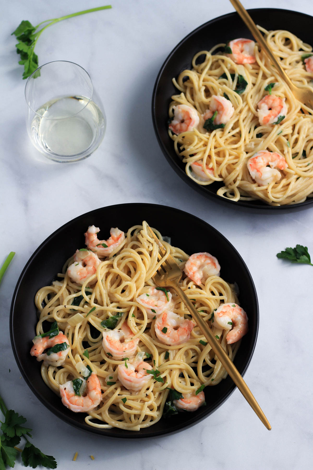 Two black bowls with creamy garlic shrimp pasta and a glass of wine to the left.