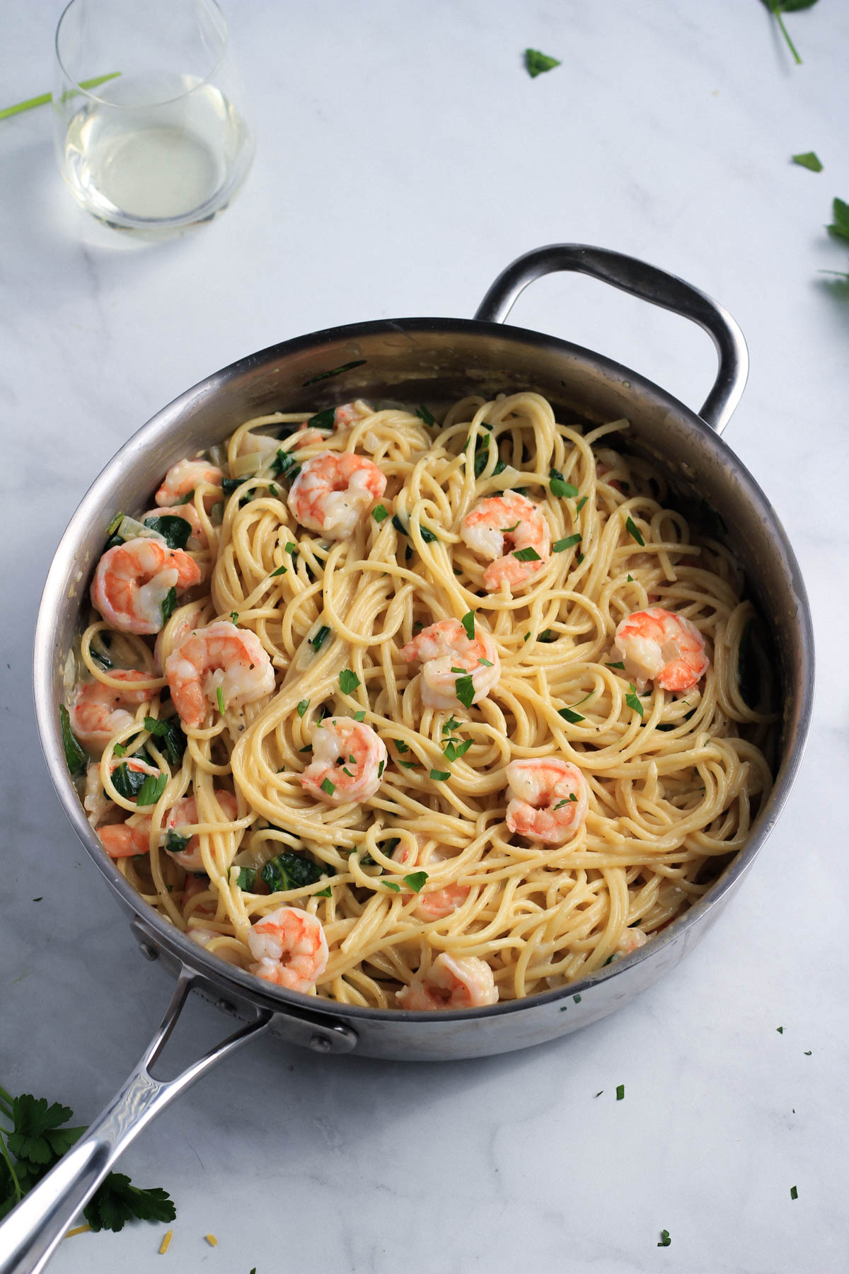 A stainless steel skillet with creamy shrimp pasta and a glass of wine in the top left.
