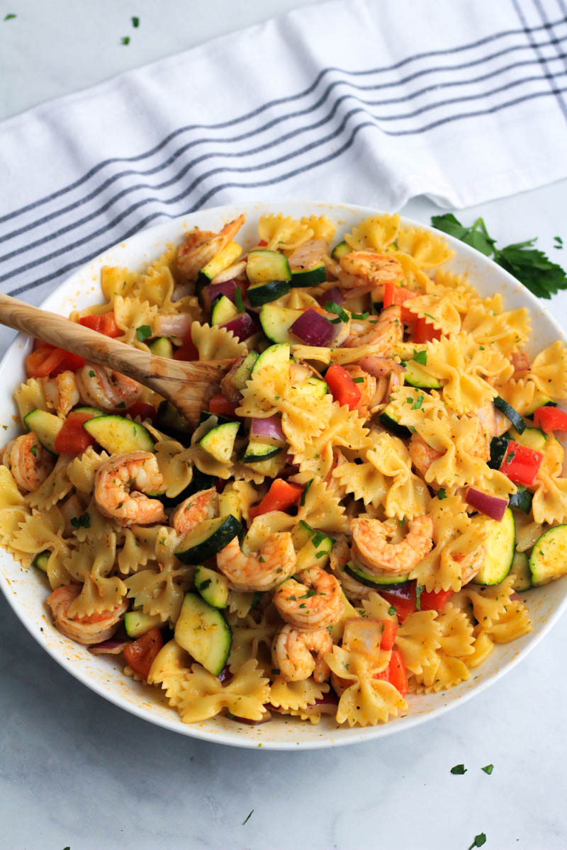 A white bowl with shrimp and vegetable pasta skillet and a large wooden spoon sticking out.
