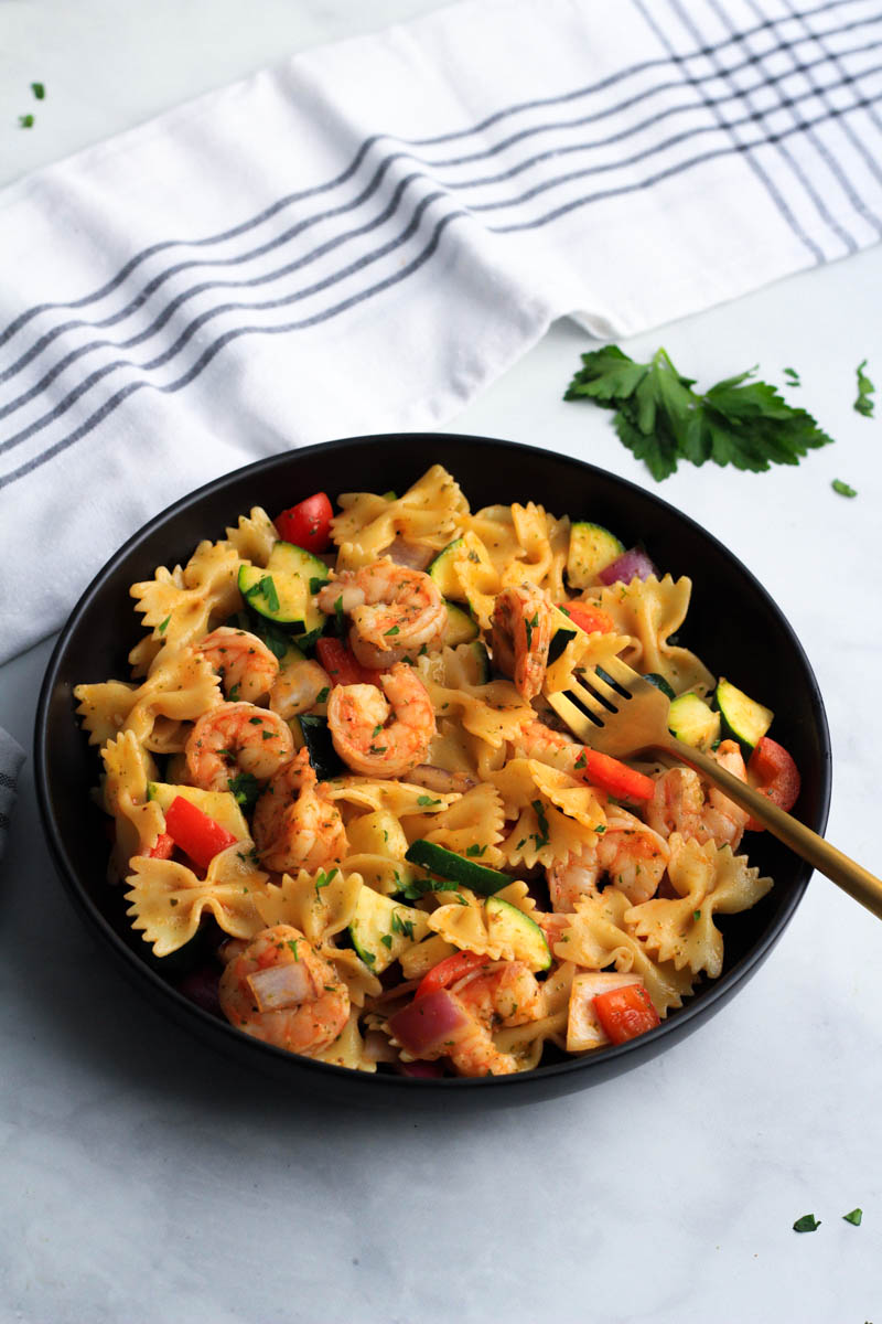 A black bowl with a gold fork sticking into the shrimp and vegetable pasta skillet dinner.