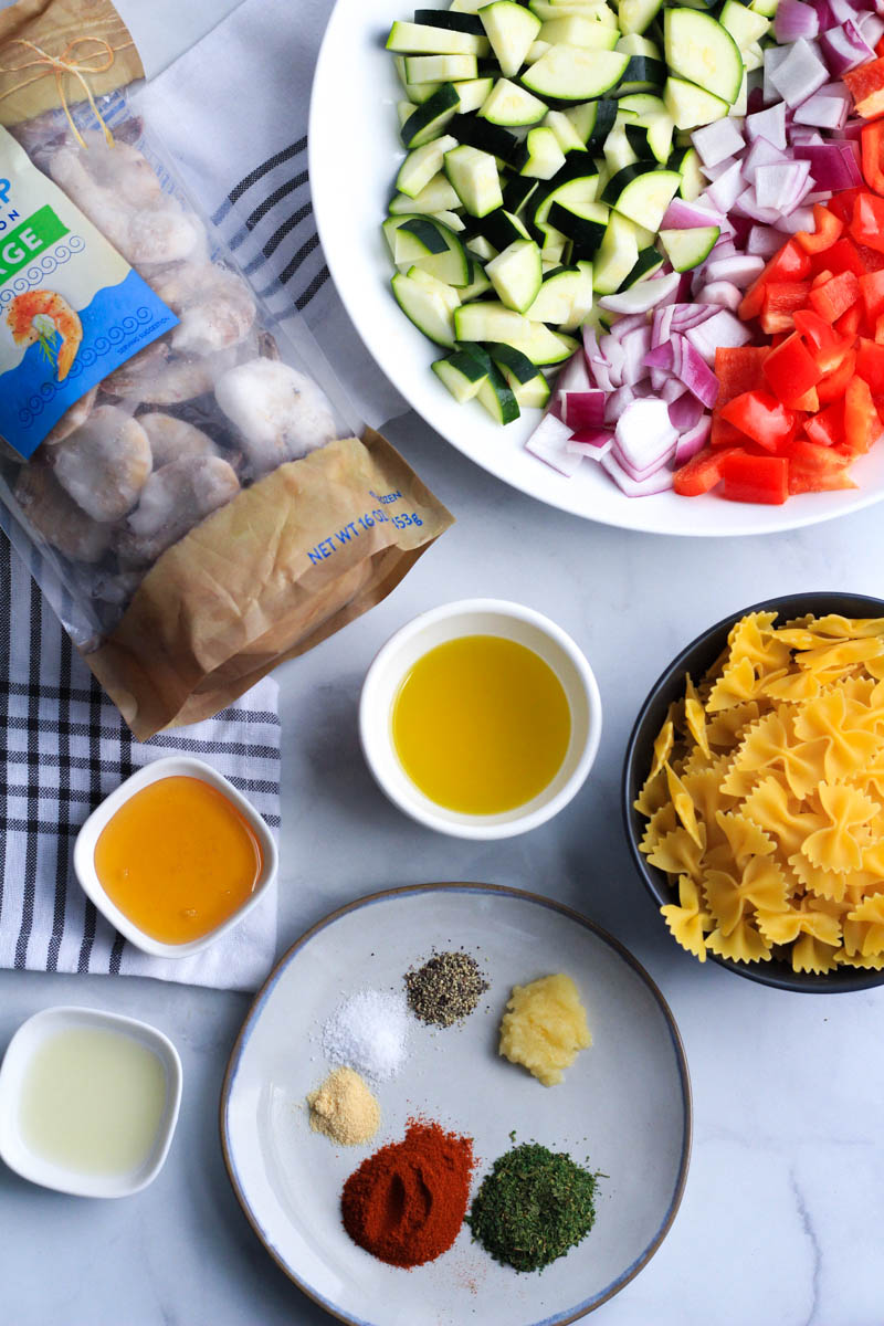 Ingredients for shrimp and vegetable pasta on a white counter.