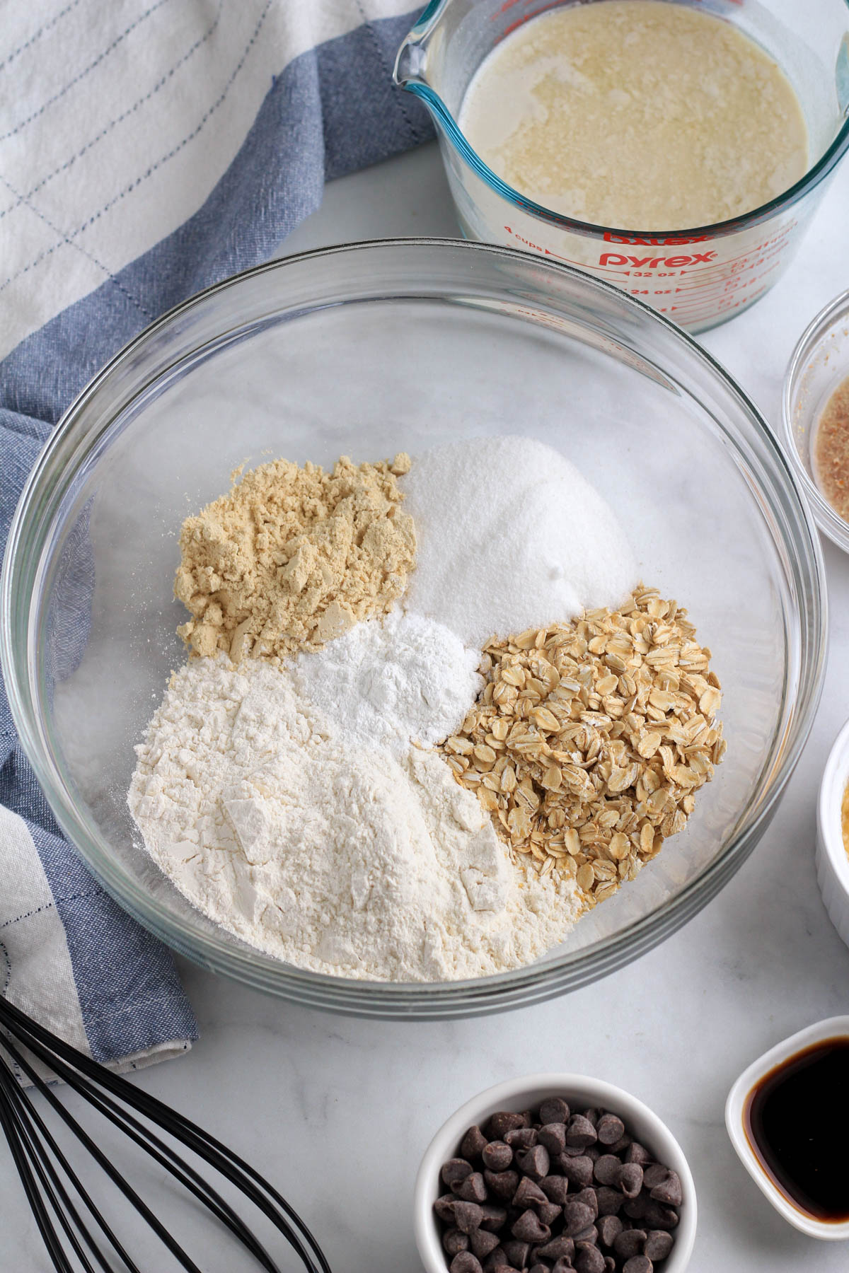 A large bowl with the dry ingredients before mixing with the remaining ingredients around the rim of the bowl.