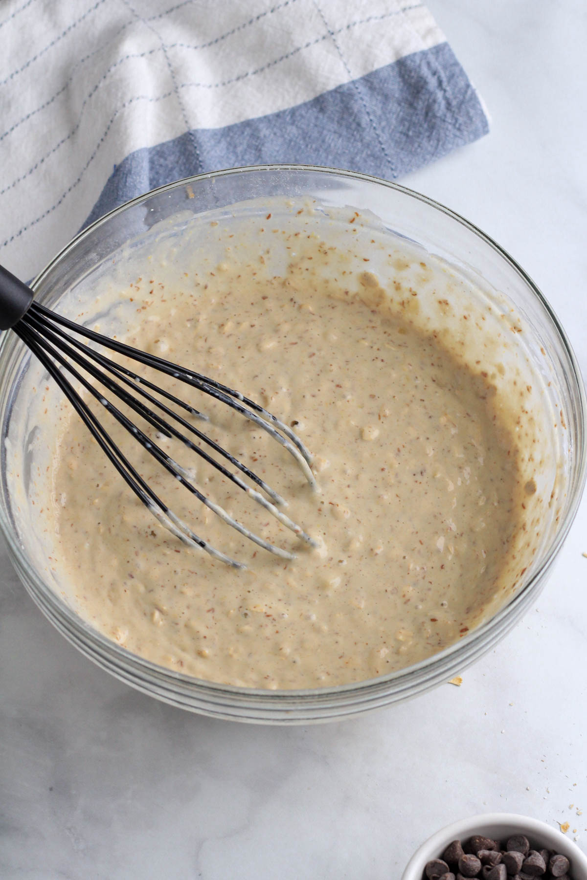 A large glass bowl with the pancake batter mixed together and a whisk in the bowl with a small bowl of chocolate chips below.
