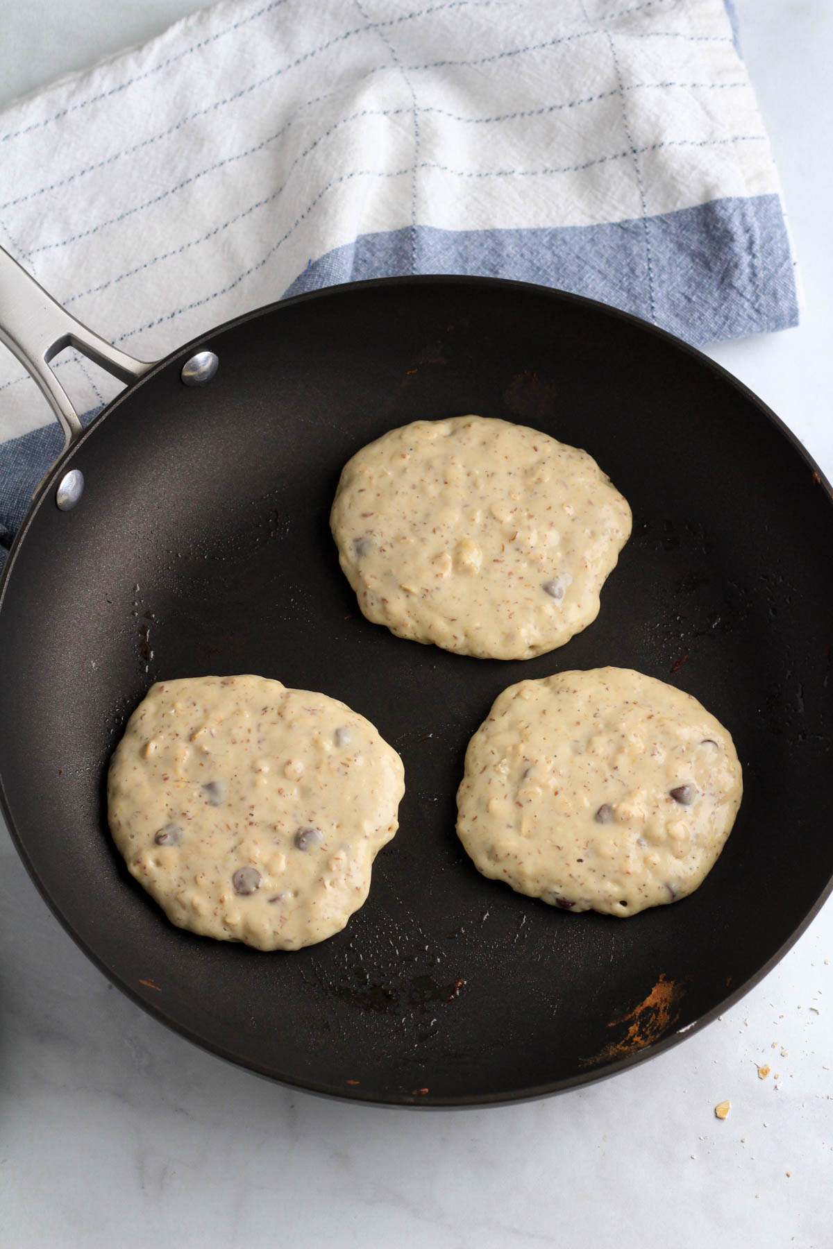 A non-stick skillet with three vanilla chocolate chip pancakes before flipping.