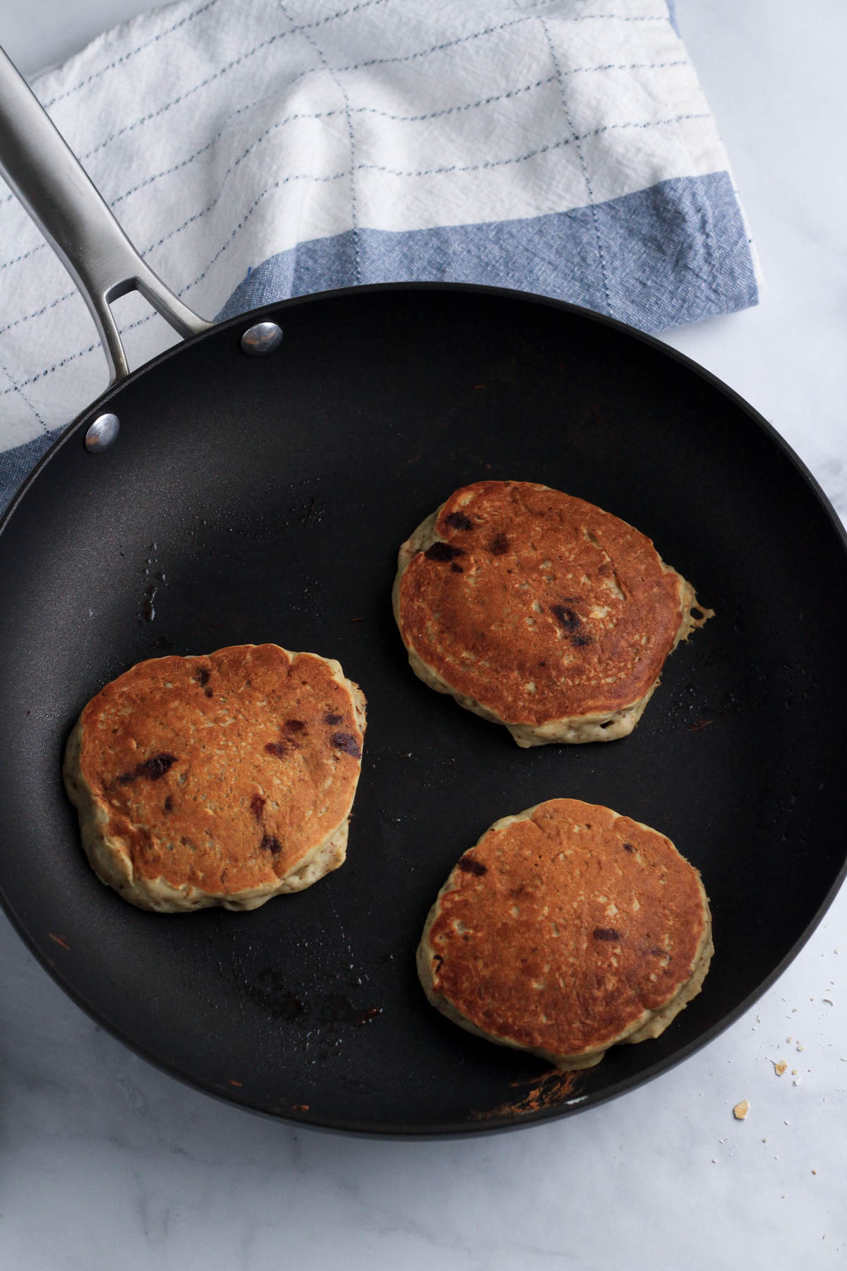 A non-stick skillet with three vanilla chocolate chip pancakes cooking.