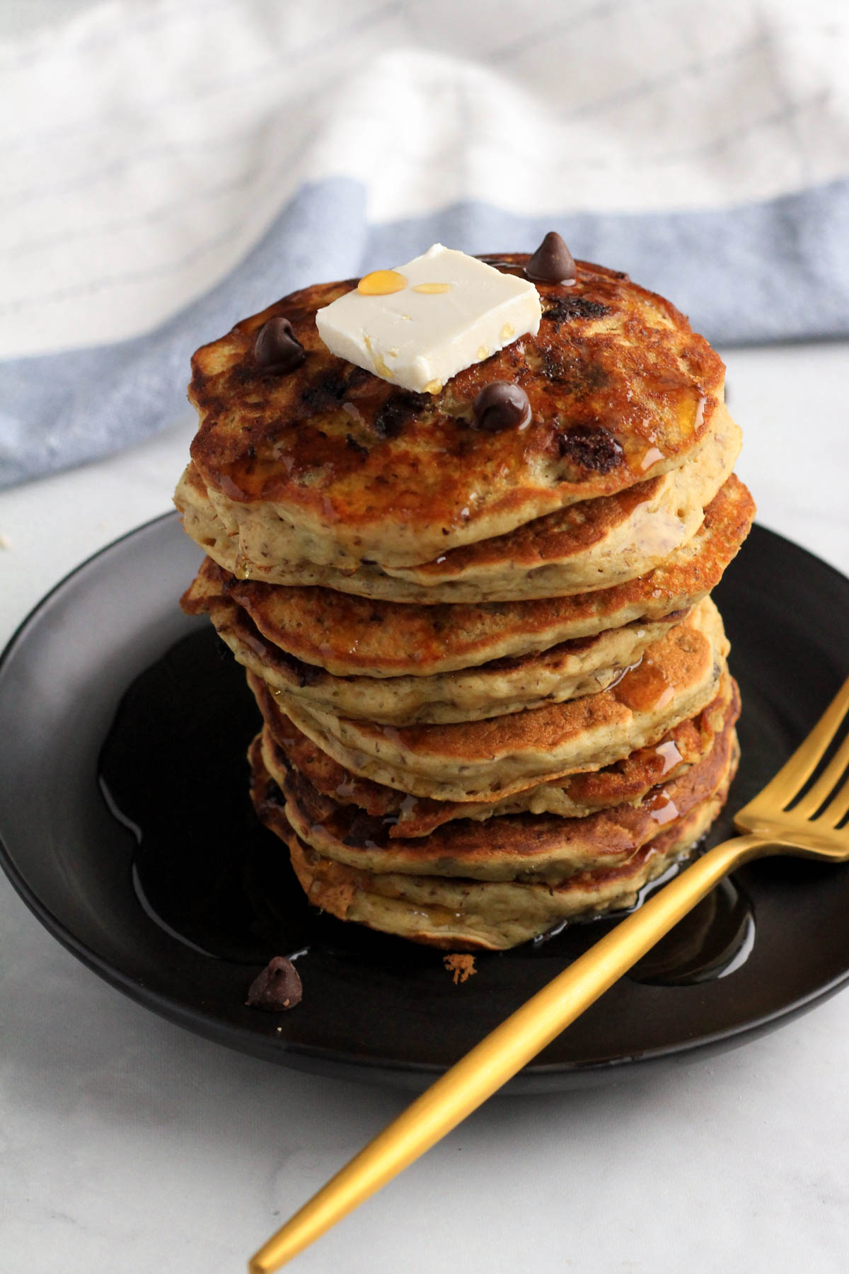 A stack of vanilla chocolate chip vegan pancakes with butter on top and a gold fork to the right.
