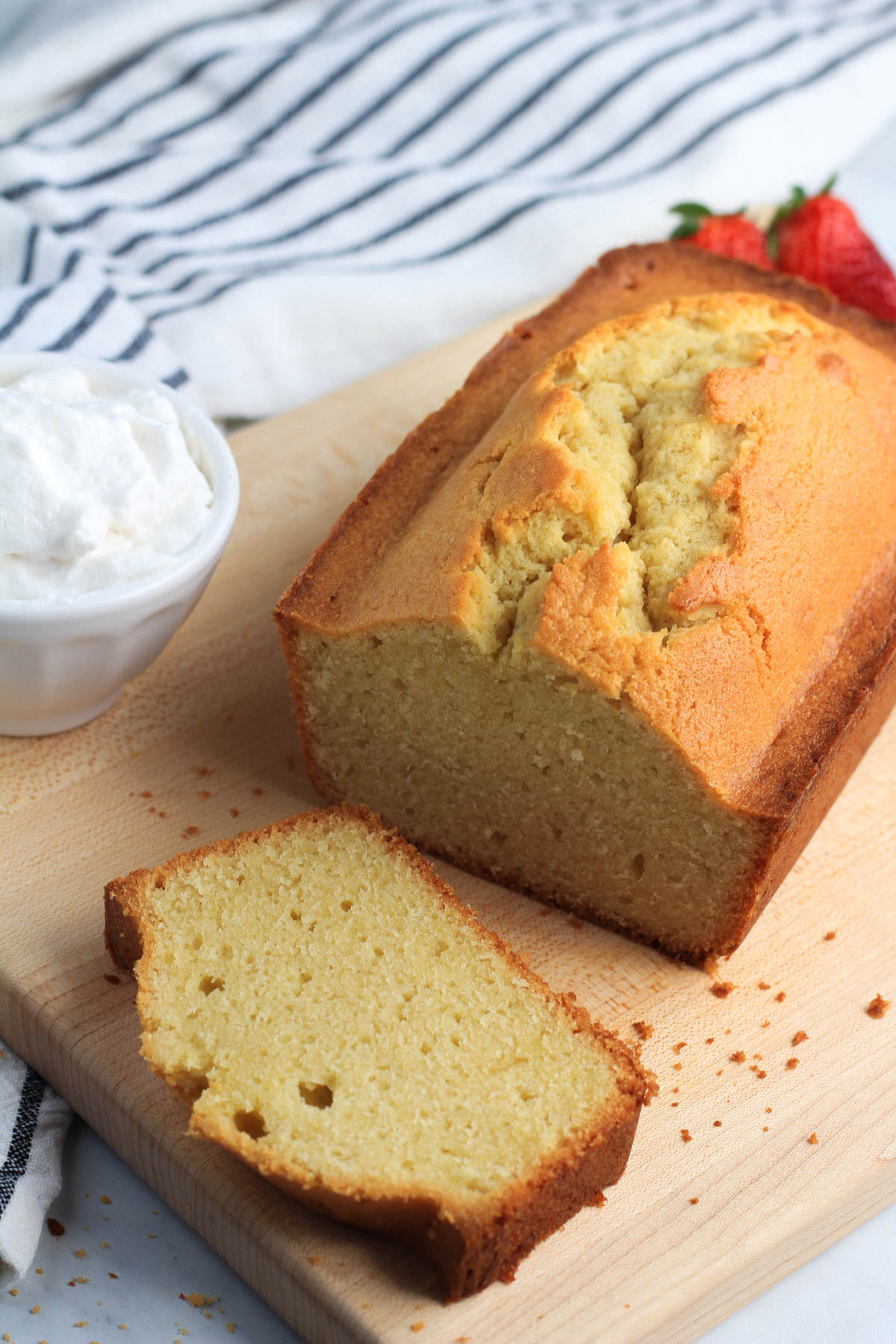 A dairy-free vanilla pound cake loaf of a wooden cutting board with one slice in the front.
