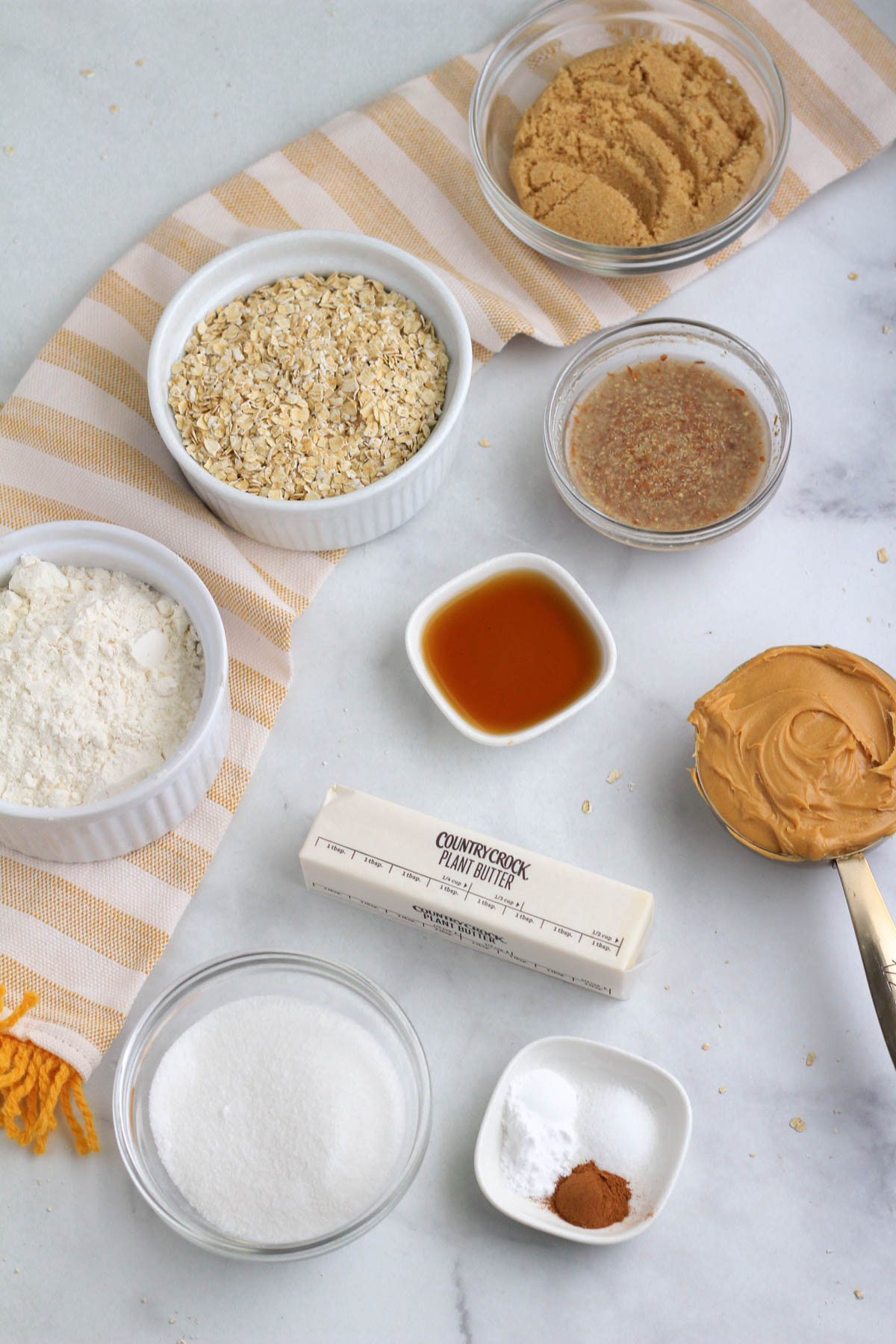 The ingredients for vegan peanut butter cookies on a white counter with a yellow and white towel.