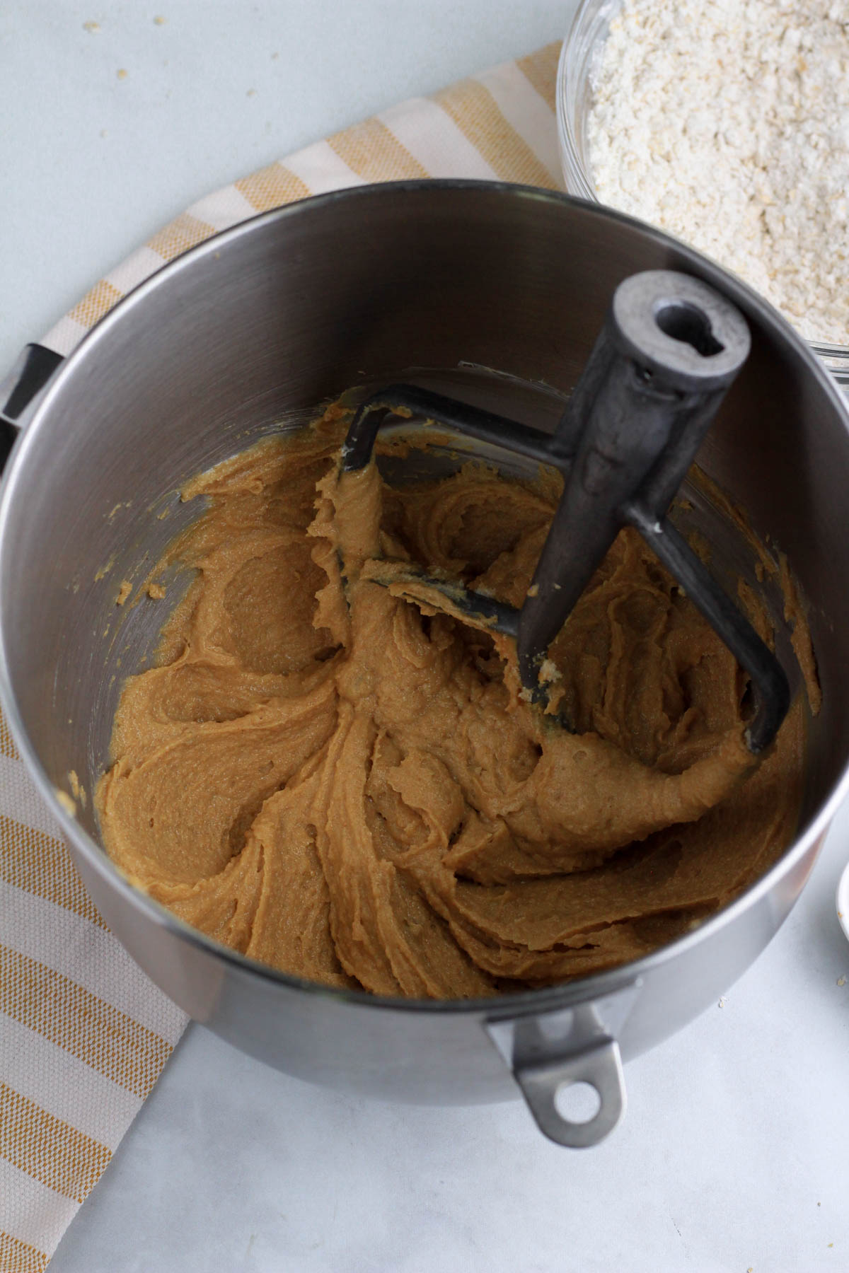 Creamed peanut butter, sugar, and vegan butter in a silver mixing bowl with a paddle attachment.