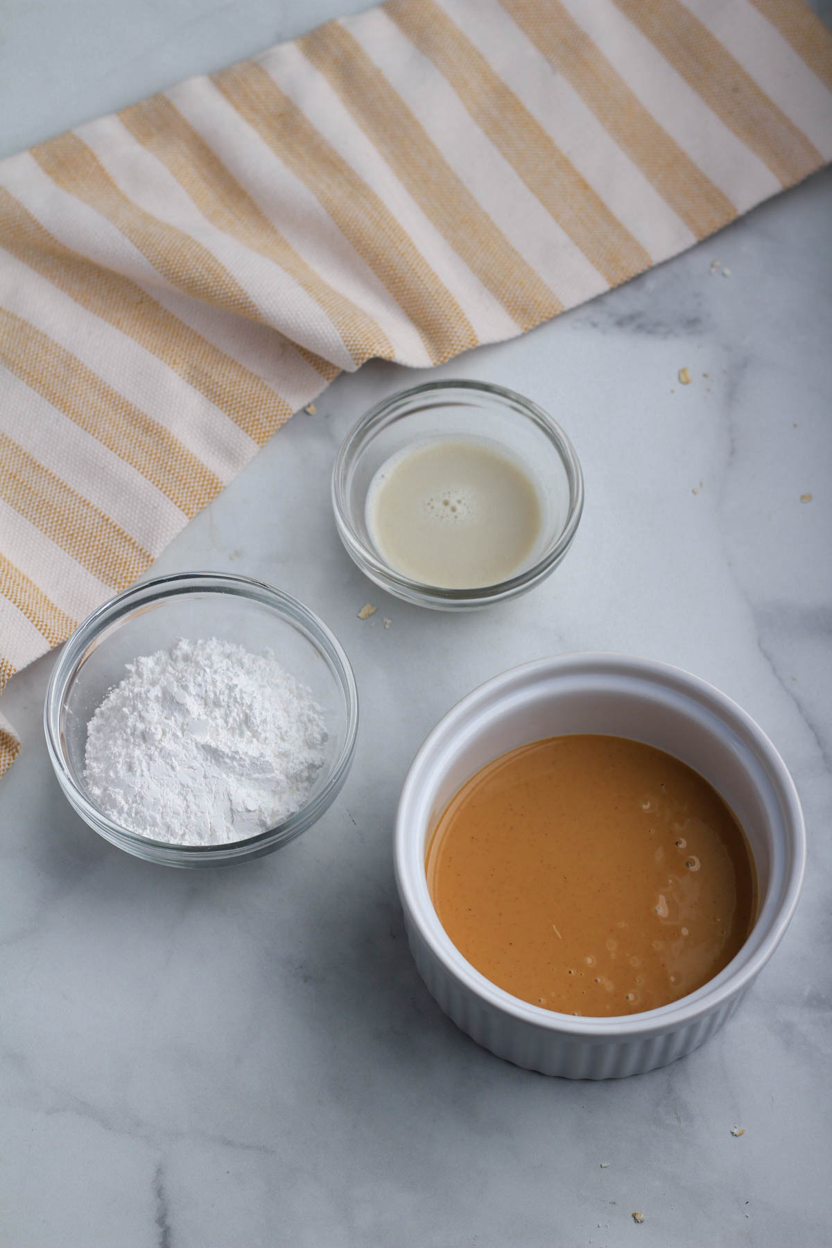 Three bowls on a counter with ingredients for peanut butter frosting.
