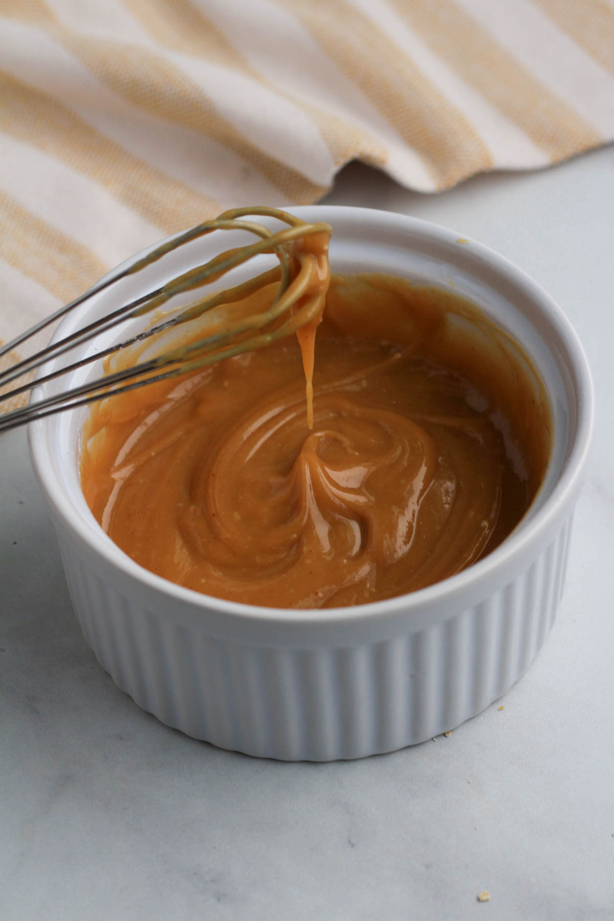 A white ramekin with a small whisk and peanut butter frosting.