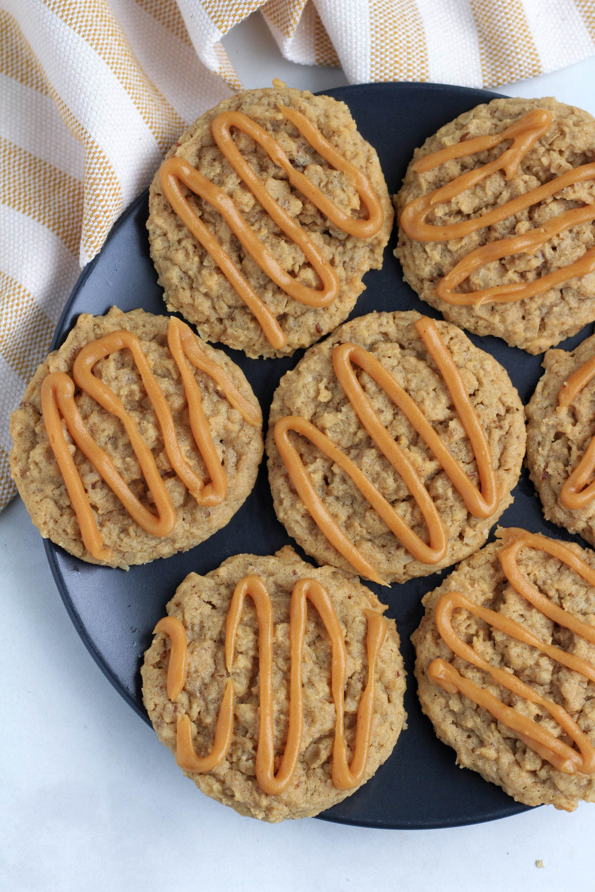 A blue plate of peanut butter oatmeal cookies with frosting on a counter with a white and yellow towel.