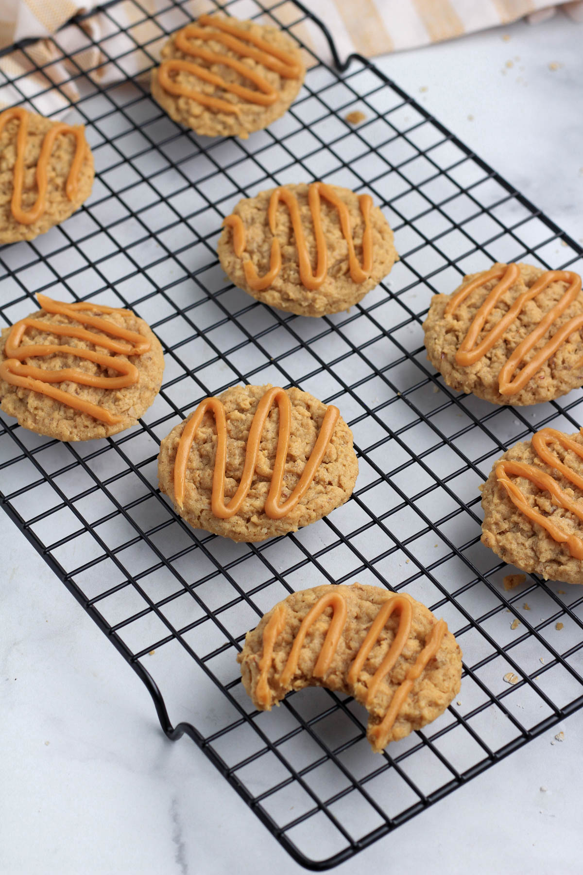 A black cooling rack with vegan peanut butter oatmeal cookies glazed with a peanut butter frosting.