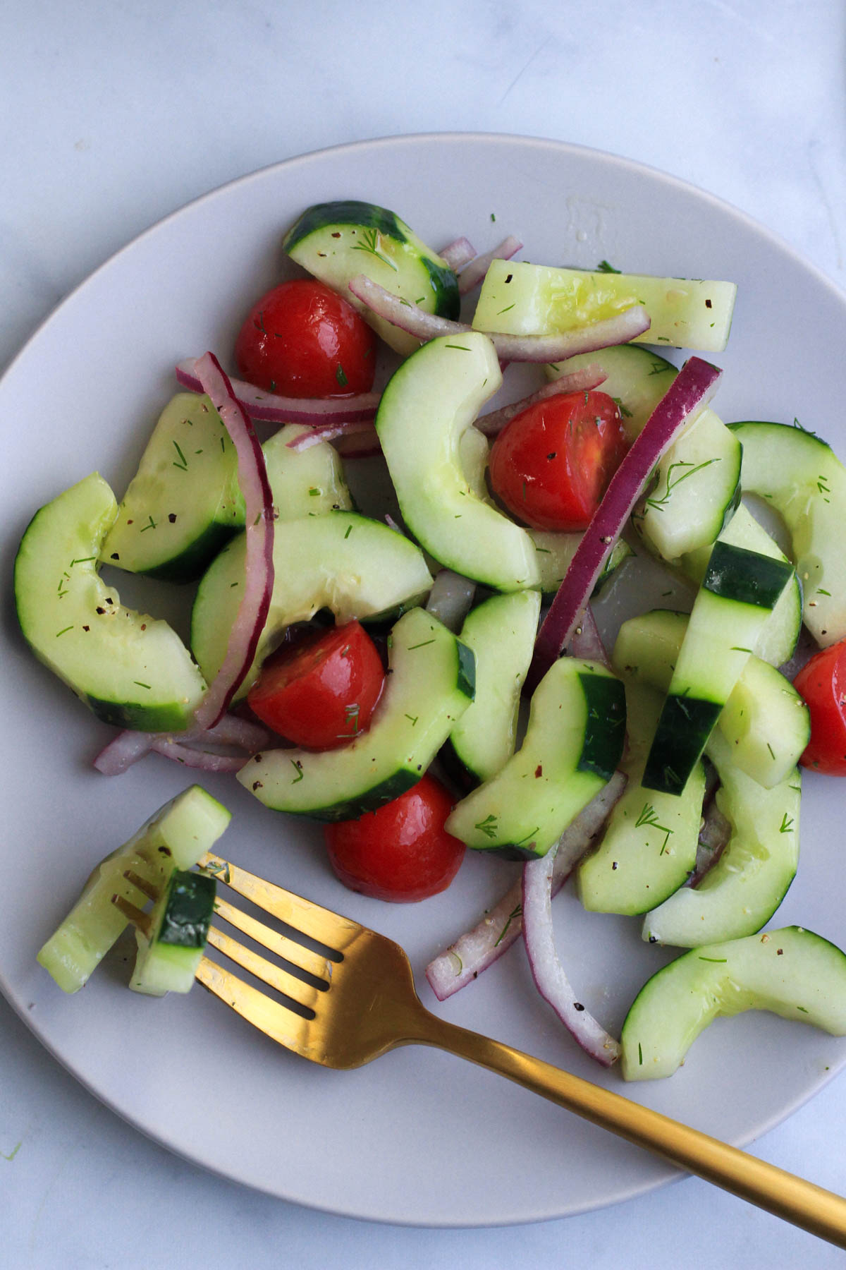 Vegan cucumber and dill salad on a white plate with a gold fork speared through two cucumber slices.