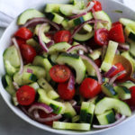 A white bowl on a white counter with cucumber, tomato, and onion salad.